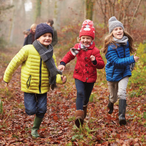 Three children running in a forest during autumn.